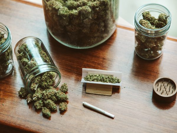 High angle view of glass jars full of marijuana plants with cannabis joint on wooden table