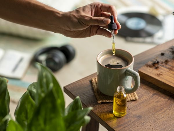 Man dropping CBD oil or Cannabis oil into a coffee cup while relaxing at home